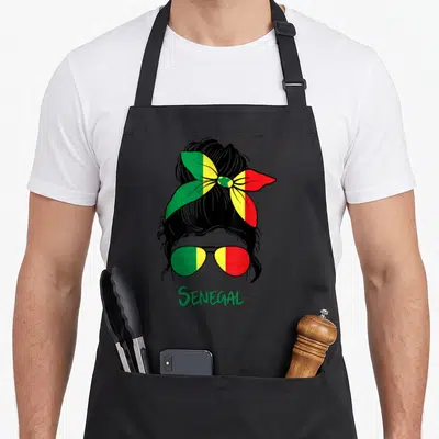Tablier de cuisine noir avec illustration d'une femme au foulard tricolore et lunettes aux mêmes couleurs.