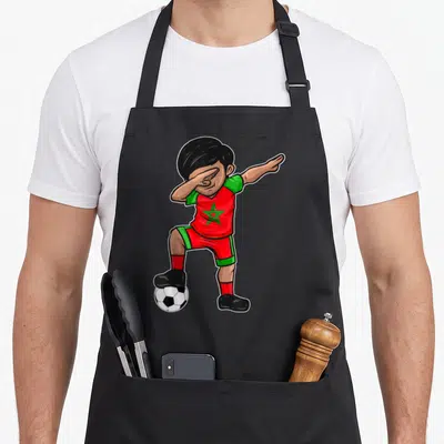 Tablier de cuisine noir avec illustration d'un footballeur marocain en train de faire un dab sur un ballon.