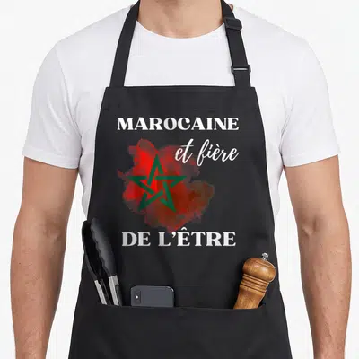 Tablier de cuisine noir avec une étoile verte sur fond rouge et les mots Marocaine et fière de l'être en typographie blanche.