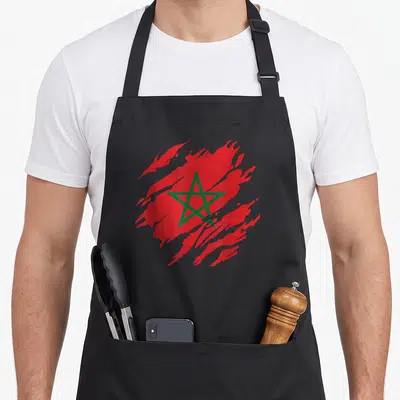 Tablier de cuisine noir avec un drapeau Maroc rouge et une étoile verte au centre dans un style graphique dynamique.