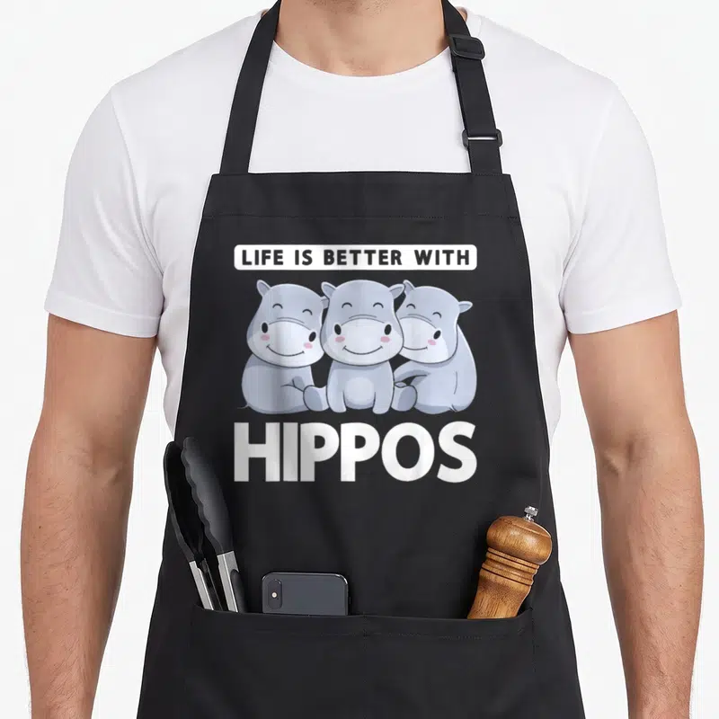 Tablier de cuisine noir avec trois hippopotames gris souriants et le texte Life Is Better With Hippos en blanc.
