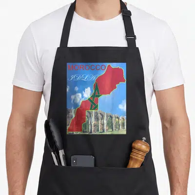Tablier de cuisine noir avec carte du Maroc rouge, étoile verte, texte Morocco et ruines d'El Jadida sur fond de ciel bleu.