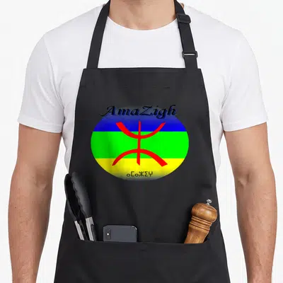 Tablier de cuisine noir avec le drapeau amazigh circulaire, le signe Tifinagh rouge et les mots AmaZigh et Tamazgha imprimés.