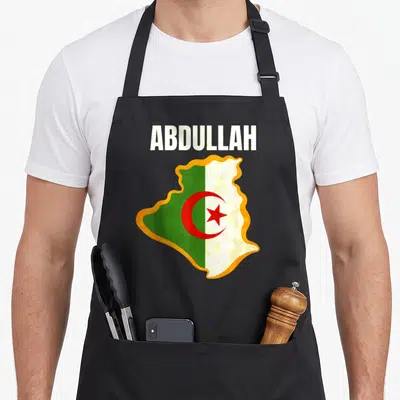 Tablier de cuisine noir avec le nom Abdullah au-dessus d'une carte de l'Algérie aux couleurs du drapeau national.