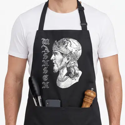 Tablier de cuisine noir avec portrait gravé de Masinsen et texte vertical stylisé en blanc.