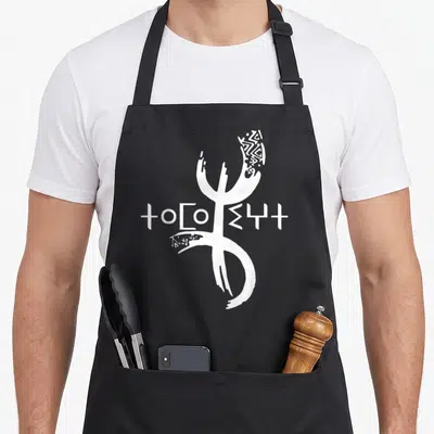Tablier de cuisine noir avec le symbole Tifinagh Yaz et des caractères amazighs blancs stylisés au centre.