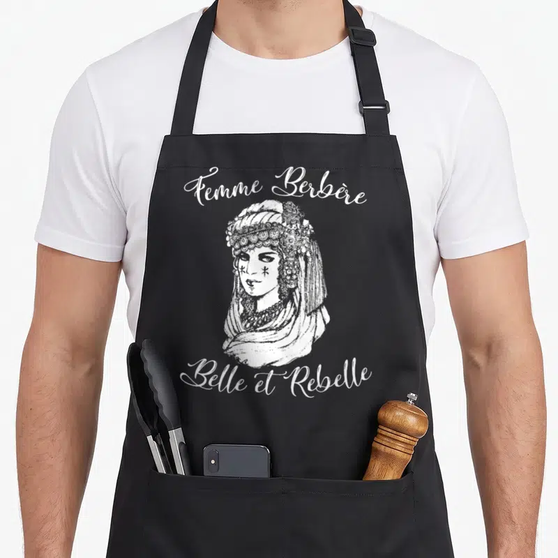 Tablier de cuisine noir avec illustration d'une femme berbère coiffée et tatouée, entourée du texte Femme Berbère Belle et Rebelle.