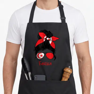 Tablier de cuisine noir avec illustration d'une femme aux lunettes au drapeau tunisien et un foulard rouge.