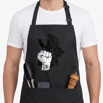 Tablier de cuisine noir avec un poing blanc levé surmonté de motifs tribaux Tifinagh noirs complexes.
