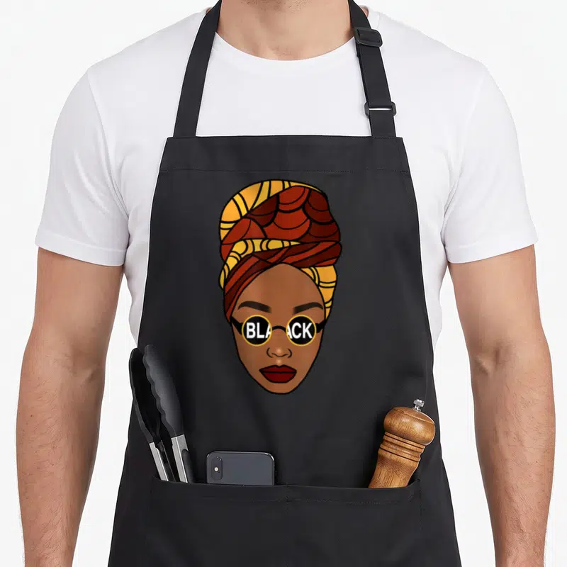 Tablier de cuisine noir avec illustration d'une femme africaine au foulard et lunettes portant l'inscription BLACK.