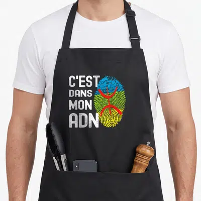 Tablier de cuisine noir avec l'inscription C'est Dans Mon ADN et un drapeau berbère stylisé en empreinte digitale.