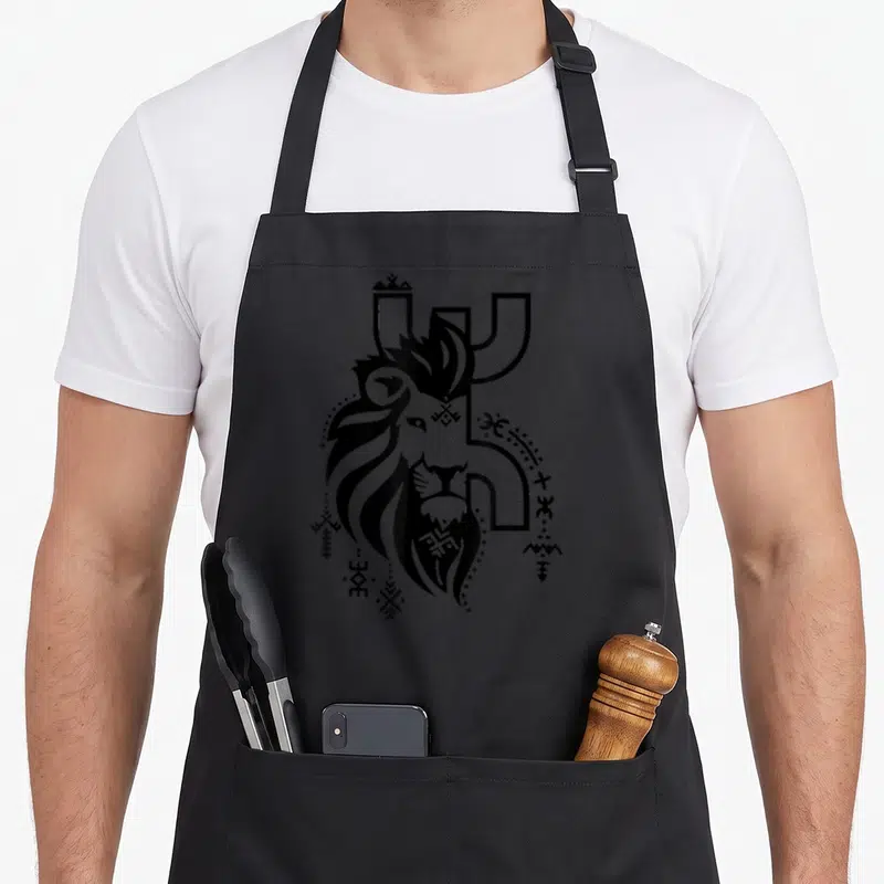 Tablier de cuisine noir avec tête de lion stylisée et symboles géométriques berbères en noir.
