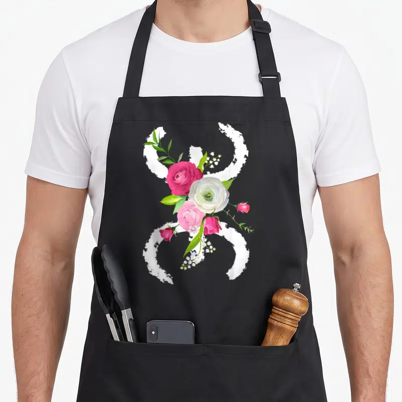 Tablier de cuisine noir avec le symbole floral berbère azigh kabyle entouré de roses roses et blanches ainsi que de feuilles vertes.