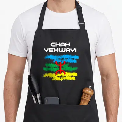 Tablier de cuisine noir avec l'inscription CHAH YEHWAYI et un signe amazigh rouge sur des bandes bleue verte et jaune.