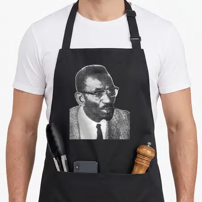 Tablier de cuisine noir avec le portrait en pointillés de Cheikh Anta Diop portant des lunettes et une cravate.
