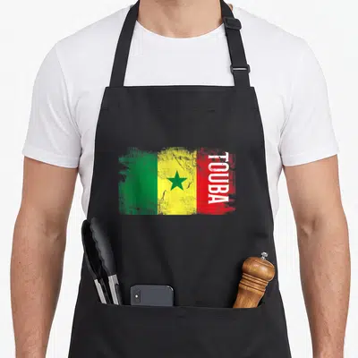 Tablier de cuisine noir avec drapeau Sénégal style brushwork et inscription TOUBA verticale blanche sur fond rouge.
