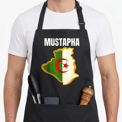 Tablier de cuisine noir avec le nom Mustapha au-dessus d'une carte de l'Algérie aux couleurs du drapeau national.