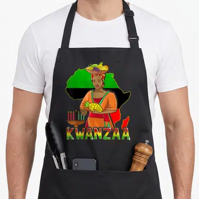 Tablier de cuisine noir avec une femme tenant un Kinara et un ananas devant une carte d'Afrique colorée.