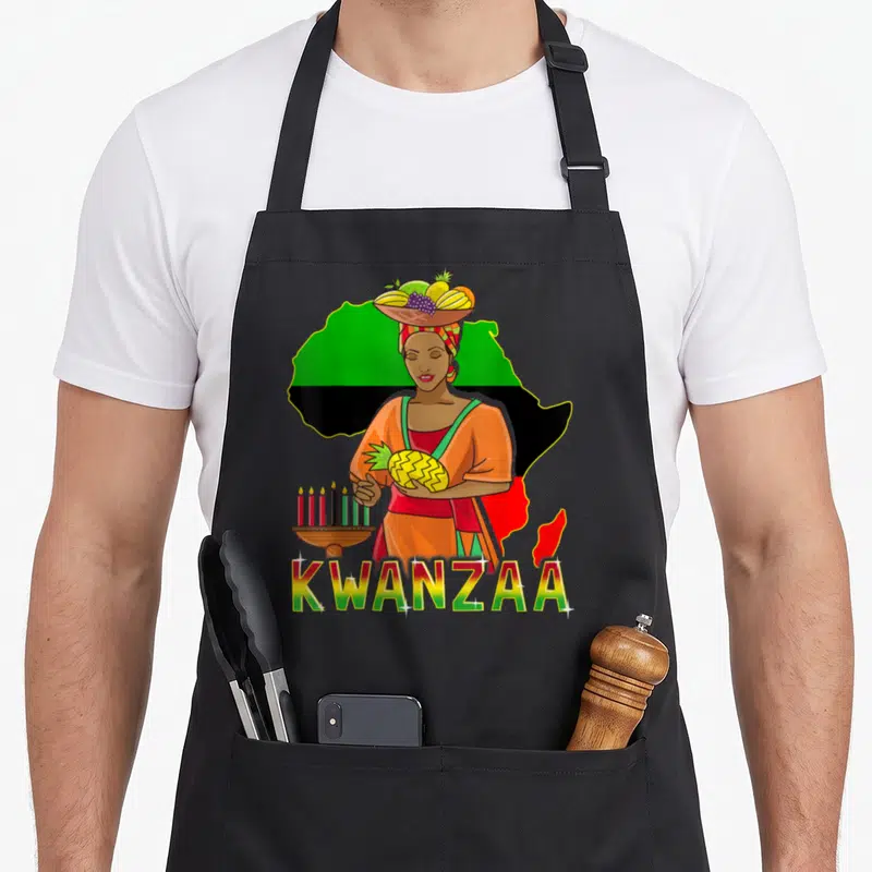 Tablier de cuisine noir avec une femme tenant un Kinara et un ananas devant une carte d'Afrique colorée.
