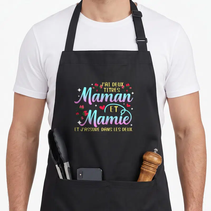 Tablier de cuisine noir avec inscription J'ai deux titres Maman et Mamie et j'assure dans les deux entourée de fleurs roses et d'étoiles.