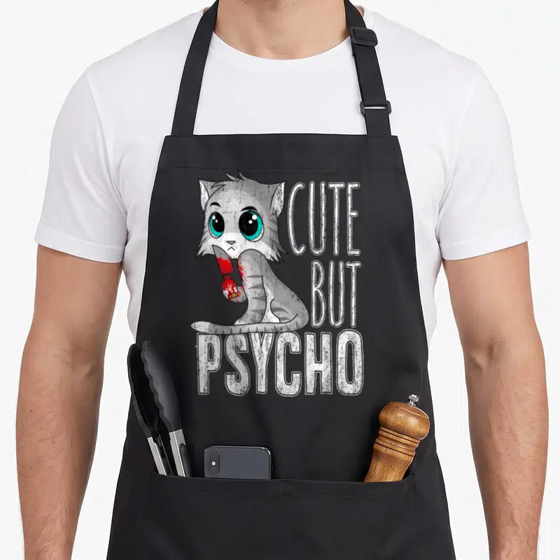 Tablier de cuisine noir avec un chat gris tenant un couteau et le texte mignon mais psycho.