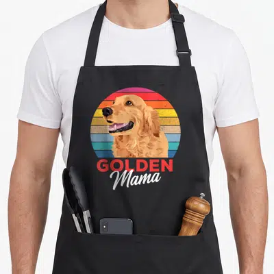 Tablier de cuisine noir avec illustration d'un golden retriever souriant et le texte Golden Mama en lettres rouges et blanches.
