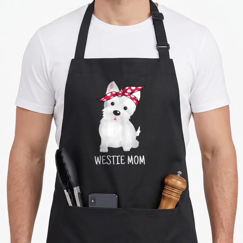 Tablier de cuisine noir avec illustration d'un chien Westie au foulard à pois rouges et texte Westie Mom en bas.