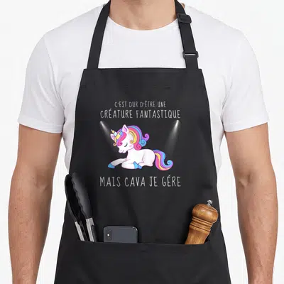 Tablier de cuisine noir avec licorne aux cheveux arc-en-ciel et texte C'est dur d'être une créature fantastique mais ça va je gère