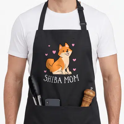 Tablier de cuisine noir avec illustration d'un chien Shiba Inu souriant et texte Shiba Mom en blanc.