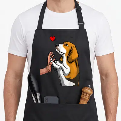 Tablier de cuisine noir avec illustration d'un beagle tenant une main humaine sous un cœur rouge vif.