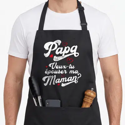 Tablier de cuisine noir avec Papa veux-tu épouser ma Maman en lettres blanches et petits cœurs rouges dispersés.