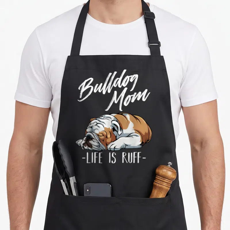 Tablier de cuisine noir avec illustration bulldog anglais dormant et texte Bulldog Mom Life Is Ruff en blanc.
