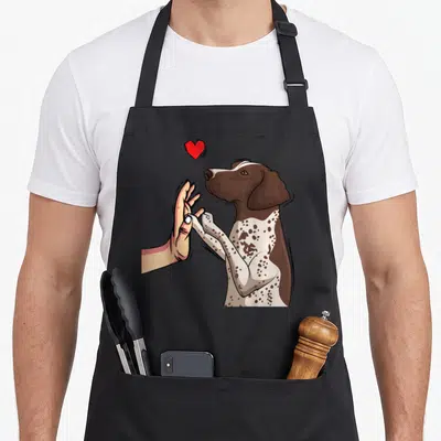 Tablier de cuisine noir avec illustration d'un chien Braque Allemand tenant une main humaine sous un cœur rouge vif.