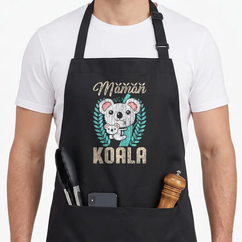 Tablier de cuisine noir avec illustration d'un koala adulte tenant un bébé koala entouré de feuilles turquoise et du texte Maman Koala en lettres beige texturées.