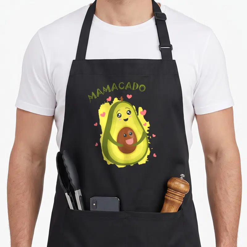 Tablier de cuisine noir avec illustration d'un avocat Mamacado enceinte entouré de petits coeurs roses et du texte vert MAMACADO au-dessus.
