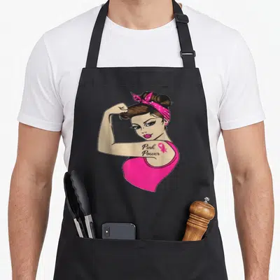 Tablier de cuisine noir avec une femme aux cheveux en chignon portant un bandeau rose et un tatouage Pink Power sur le bras.