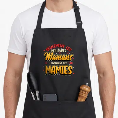 Tablier de cuisine noir orné d'un graphisme coloré affichant le texte « Seulem ent les meilleures Mamans deviennent des Mamies » entouré de cœurs rouges.