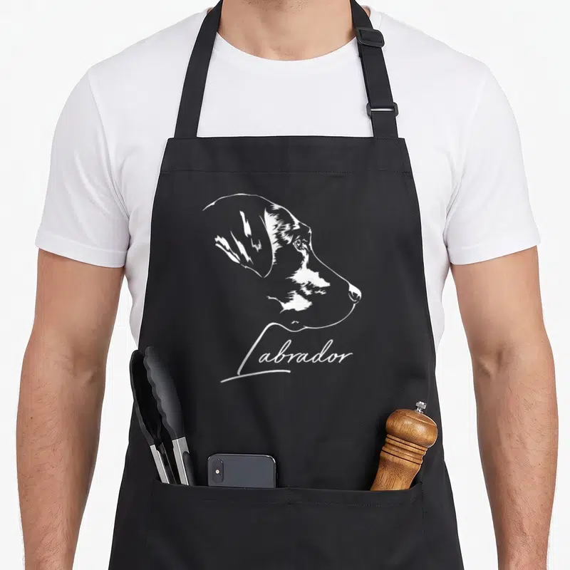 Tablier de cuisine noir avec portrait stylisé blanc de Labrador Retriever et l'inscription Labrador en calligraphie sous le museau.