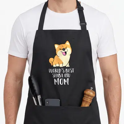 Tablier de cuisine noir avec un Shiba Inu cartoon souriant et le texte blanc World's Best Shiba Inu Mom