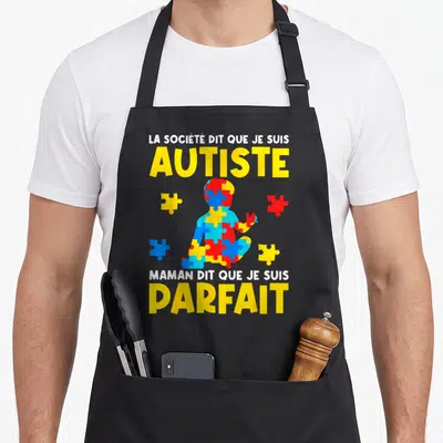 Tablier de cuisine noir avec silhouette enfantine formée de pièces de puzzle multicolores et texte jaune blanc sur fond sombre.