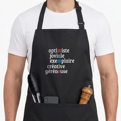Tablier de cuisine noir avec les mots optimiste, joviale, exemplaire, créative et généreuse imprimés en blanc et couleurs.