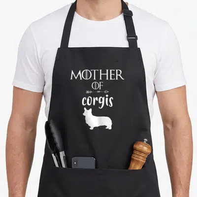Tablier de cuisine noir avec inscription Mother of Corgis et silhouette de corgi en blanc.