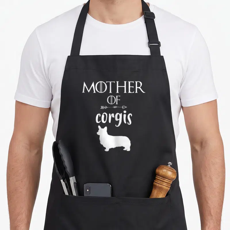 Tablier de cuisine noir avec inscription Mother of Corgis et silhouette de corgi en blanc.