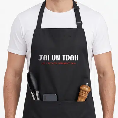 Tablier de cuisine noir avec l'inscription J'ai un TDAH en blanc et une phrase en rouge.