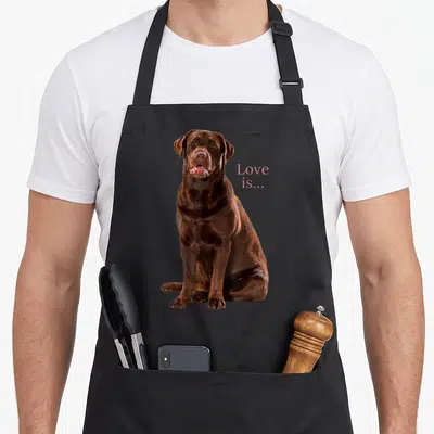 Tablier de cuisine noir avec illustration d'un Labrador Retriever chocolat et texte Love is en rose.