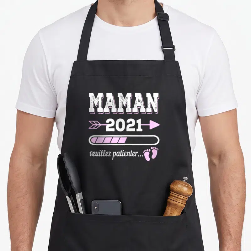 Tablier de cuisine noir avec texte maman 2021 veuillez patienter et icônes roses.