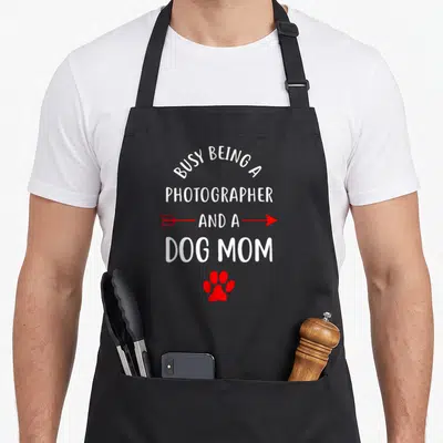 Tablier de cuisine noir avec texte blanc et flèche rouge ainsi qu'une patte de chien rouge en bas du motif imprimé.
