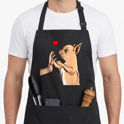 Tablier de cuisine noir avec illustration d'un chihuahua tenant une main humaine sous un cœur rouge vif.