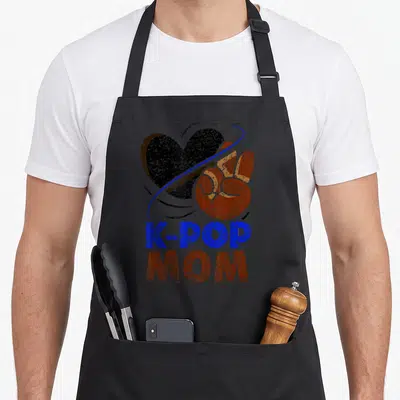 Tablier de cuisine noir avec inscription K-POP MOM, cœur noir et geste de main orange sur fond uni.