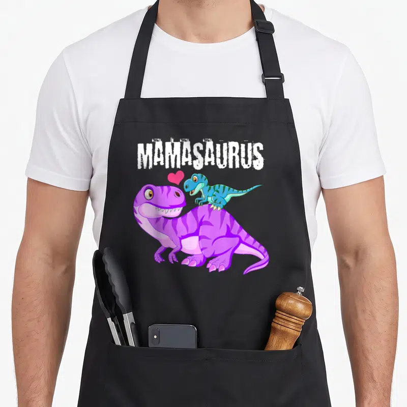 Tablier de cuisine noir avec dinosaure violet portant un bébé Rex bleu et le texte Mamasaurus en blanc.
